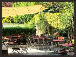 Biergarten mit Tischen unter Sonnenschirm vor grüner Hecke